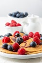 Close-up of pancakes with caramel on plate with blueberries and raspberries with bowls and jar on white table, Royalty Free Stock Photo