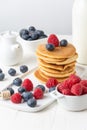 Close up of pancakes in stack with blueberries, raspberries and milk on table and white background, vertical, Royalty Free Stock Photo