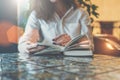 Close-up of paper book, notebook, diary on table in cafe. Businesswoman in white shirt sitting at table and reading book