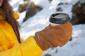 Close-up paper cup with a black lid in the hands of a woman in mittens