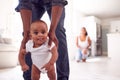 Close Up Of Parents Encouraging Smiling Baby Daughter To Take First Steps And Walk At Home