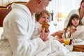 Enjoy the taste. Close up of parents and two kids in white bathrobes having breakfast in bed, eating and drinking in Royalty Free Stock Photo