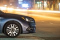 Close up of parked car on roadside at night with blurred view of traffic lights of moving vehicles on city street Royalty Free Stock Photo