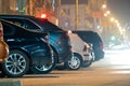 Close up of parked cars on roadside at night with blurred view of traffic lights of moving vehicles on city street Royalty Free Stock Photo