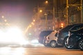 Close up of parked cars on roadside at night with blurred view of traffic lights of moving vehicles on city street Royalty Free Stock Photo
