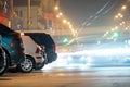 Close up of parked cars on roadside at night with blurred view of traffic lights of moving vehicles on city street Royalty Free Stock Photo