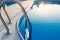 Close-up of a part of swimming pool with a stainless steel ladder and blue water on sunset. Summer vacation, holidays, relax Royalty Free Stock Photo