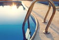 Close-up of a part of swimming pool with a stainless steel ladder and blue water on sunset. Summer vacation, holidays, relax, Royalty Free Stock Photo