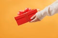 Close-up partial view of man in sweater holding red gift box on yellow background.Gift giving concept Royalty Free Stock Photo