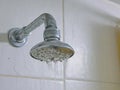 Close up of a partly clogged shower head in a bathroom, causing it to putting out so little water