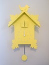 Close up of pastel yellow wooden cuckoo clock mounted on gray interior wall