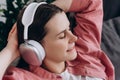 Close up of peaceful happy relaxed young woman wearing headphones listening to music, leaning back on couch at home, mindful calm