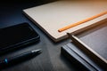 Close up pen placed on black notebook, brown notebook, smartphone and pencil on black desk background in dramatic lighting tone. C Royalty Free Stock Photo