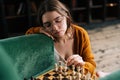 Close-up of pensive cute young woman wearing elegant eyeglasses making chess move with knight piece sitting in wooden Royalty Free Stock Photo