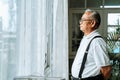 Close up of pensive old man with glasses looking out of window feeling lonely. 70s Asian pensioner missing children and Royalty Free Stock Photo