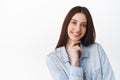 Close up of pensive smiling girl, touch chin, showing pure clean perfect skin, white smile teeth, standing against Royalty Free Stock Photo