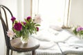 Close up of peonies in a vase on a vintage wooden chair. Rustic style interior with mattresses, pillows and flowers near an open