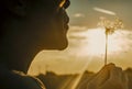 Close up of people blowing big dandelion flower with sunset light and field in background. Outdoor leisure activity and nature Royalty Free Stock Photo