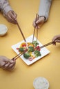 Close up of people holding chopsticks and sharing one dish