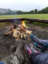A close up of 3 people in pairs of Wellington boots sitting around a campfire