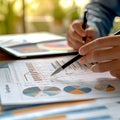 Close-up of a person analyzing financial charts and graphs, pen in hand, on a digital tablet, with paper documents on Royalty Free Stock Photo