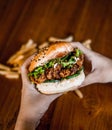 A close-up of a person holding a half-eaten hamburger with cheese, lettuce, tomato, onion, and french fries Royalty Free Stock Photo