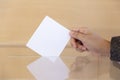 Close up of a person`s hand inserting a blank envelope into a ballot box.