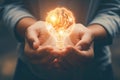 A close-up of a person\'s hands holding a glowing brain shaped light bulb, representing innovative ideas