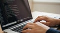 Close-up of a persons hands typing on a laptop keyboard with lines of code displayed on the screen Royalty Free Stock Photo
