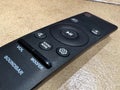 Close-Up and Perspective View of a Black Remote Control for a Soundbar Featuring Buttons for Volume, Woofer, Pairing, and Sound