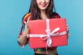 Close-up pf beautiful young brunette girl holding a red gift box in her hands while standing against a blue background