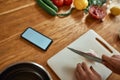 Close up of phone with blank screen on the table. Man cutting onion on chopping board, using smartphone app while Royalty Free Stock Photo