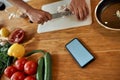 Close up of phone with blank screen on the table. Man cutting onion on chopping board, using smartphone app while Royalty Free Stock Photo