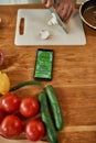 Close up of phone and vegetables on the table. Man cutting onion on chopping board, using smartphone app while cooking Royalty Free Stock Photo