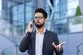 Close-up photo of an angry and sad young Indian man in a business suit standing on the street near an office center and Royalty Free Stock Photo