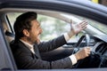 Close-up photo of angry young businessman in suit driving car and emotionally gesturing with hands, displeased shouting Royalty Free Stock Photo