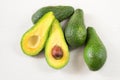Close-up photo of avocados cut to half, brown seeds visible, with more avocados on white wooden background.