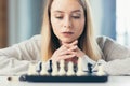 Close-up photo of a blonde woman playing chess, thoughtfully making a move