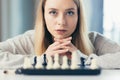 Close-up photo of a blonde woman playing chess, thoughtfully making a move