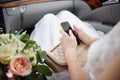 Close-up photo of bride sitting in car and holding her smartphone during her wedding day