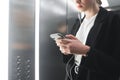 Close up photo of a busy young woman using smartphone in the elevator. Ambitious office worker texting by her phone and using