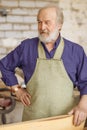 Close up photo of cheerful old joiner holding woodenplank workstation