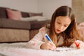 Close up photo of a child with long blond hauir seriosly and attentively writing on the paper with a pen lying down on Royalty Free Stock Photo