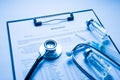 Close up photo of clipboard with stethoscope glass vial and syringe lying on doctors desktop