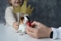 Close up photo of cute guinea pig eating cherry tomato from cropped woman hand. Little girl hold toy crown under pet