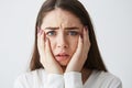 Close up photo of displeased frightened girl looking at camera touching face frowning over white background.