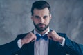 Close up photo of elegant man looking into mirror correcting his bowtie wearing blazer jacket  over grey Royalty Free Stock Photo