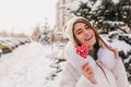 Close-up photo of enchanting long-haired girl walking on snowy street with lollipop. Pretty laughing woman in knitted Royalty Free Stock Photo