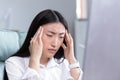 Close up photo. Exhaustion at work. A young Asian woman holds her head, feels pain, grimaces. Royalty Free Stock Photo