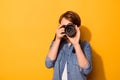 Close up photo of female photographer photographing with a camera in casual clothes on the bright yellow background